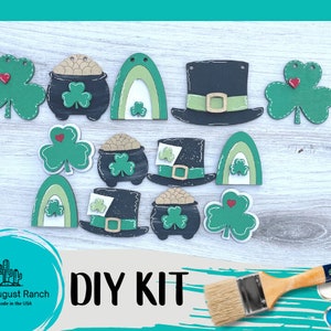 May include: A DIY kit featuring wooden St. Patrick's Day themed cutouts. Includes green shamrocks, pots of gold, rainbows, and top hats. The kit is designed for crafting and includes the text "DIY KIT".
