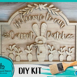 May include: DIY wood sign kit featuring a bunny rabbit and carrots. The sign reads "Welcome to our Carrot Patch". The kit includes a paintbrush and paint pots.
