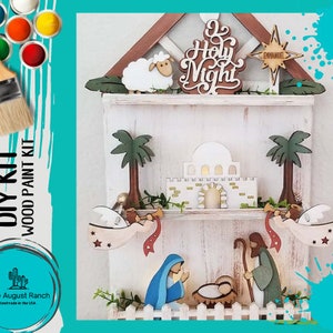 May include: DIY wood paint kit featuring a nativity scene with angels, a sheep, and the words "O Holy Night" and "Emmanuel." The kit includes a brush and paint pots. Handmade in the USA.