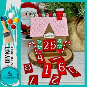 May include: DIY kit for a wooden Christmas countdown house with a pink roof, candy cane accents, and numbered tiles. The kit includes paint and instructions.