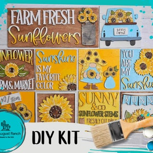 May include: DIY craft kit featuring nine wooden signs with sunflower and farmhouse themes. The signs include phrases like "Farm Fresh Sunflowers", "Sunshine is my favorite color", and "You are my Sunshine". The kit also includes a paintbrush and paint pots.