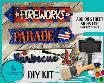 Puede incluir: Kit de bricolaje para tres letreros de madera con las palabras "Fuegos artificiales", "Desfile" y "Barbacoa" pintadas en rojo, blanco y azul. El kit incluye pintura y un pincel. Los letreros están diseñados para ser utilizados con un marco de poste alto.