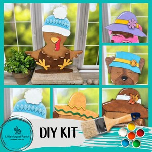 May include: DIY craft kit featuring five wooden cutouts of animals wearing hats. The kit includes a paintbrush and a set of acrylic paints in various colors. The animals include a turkey, a pig, a dog, a bear, and a scarecrow. The text "DIY KIT" is displayed on the image.