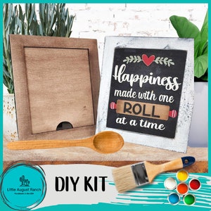 May include: DIY kit for a wooden sign that says "Happiness made with one roll at a time". The kit includes a wooden sign, paint, a paintbrush, and a wooden spoon.