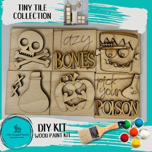 May include: A DIY wood paint kit with six wooden tiles featuring Halloween-themed designs. The tiles include a skull and crossbones, a pumpkin, a Frankenstein face, a potion bottle, and the text "lazy bones" and "pick your poison".