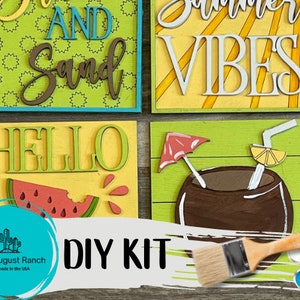 May include: DIY kit for painting four wooden signs with summer themes. The signs feature the phrases "Sun and Sand", "Summer Vibes", "Hello", and a tropical drink with an umbrella. The kit includes paint, brushes, and instructions.