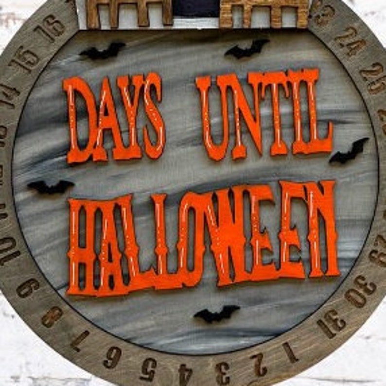 May include: A wooden countdown clock with a gray background and orange text that reads "Days Until Halloween". The clock has black bats and a black silhouette of a house on the top.