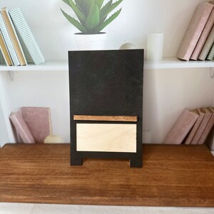 K&ouml;nnte beinhalten: Eine schwarze Tafel mit einem Holzrahmen und einem kleinen Regal. Die Tafel hat einen wei&szlig;en Hintergrund und ein Holzregal.