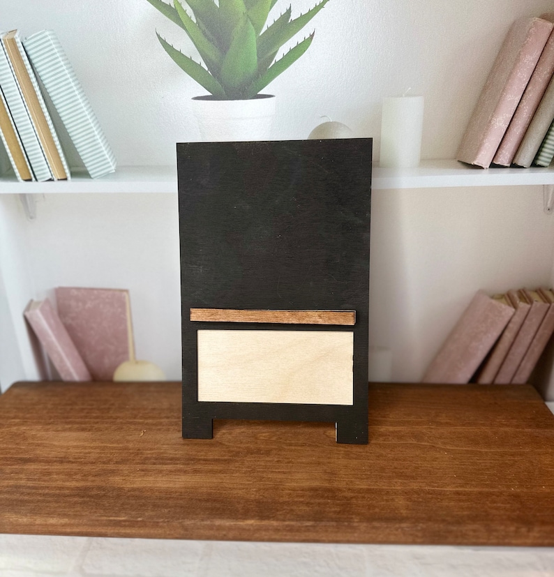K&ouml;nnte beinhalten: Eine schwarze Tafel mit einem Holzrahmen und einem kleinen Regal. Die Tafel hat einen wei&szlig;en Hintergrund und ein Holzregal.