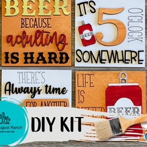 May include: DIY craft kit for making four wooden signs with beer-themed sayings. The signs feature phrases like "Beer because adulting is hard" and "It's 5 o'clock somewhere". The kit includes paint, brushes, and stencils.