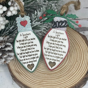 May include: Two wooden lightbulb ornaments with a red heart and green holly leaves. The ornaments have a poem on them that reads "A Teachers Light This little light is for you teacher, To hang upon your tree When you see it swing and sway I hope you'll think of me Your light has taught me how to shine. Your light has helped me grow. You've set me on a brighter path I hope you always know!"