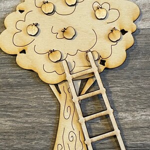 May include: A wooden apple tree with a ladder. The tree has seven apples on it. The tree and ladder are both unfinished and ready to be painted.