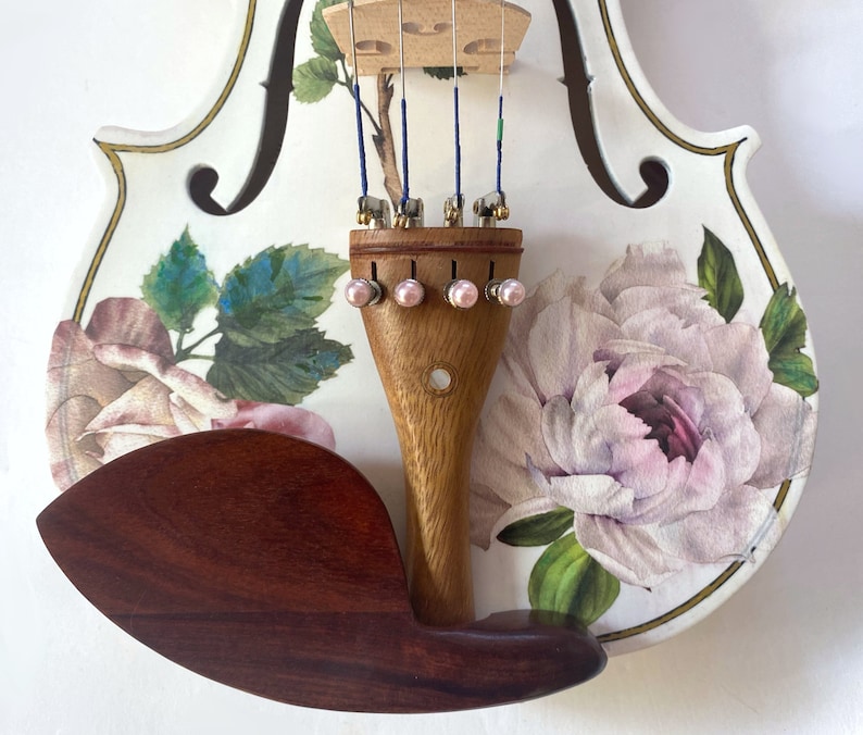 Pu&ograve; includere: Un violino bianco con un design floreale con rose rosa e foglie verdi. Il violino ha un manico in legno e un poggiamento per il mento marrone.