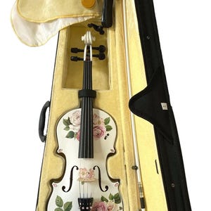 A white violin with a floral pattern on its body is displayed in a yellow violin case with a black handle.