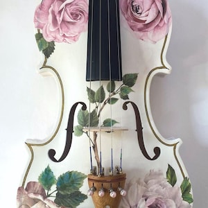 A white violin with a floral design on the body and a black neck, featuring pink roses and green leaves.