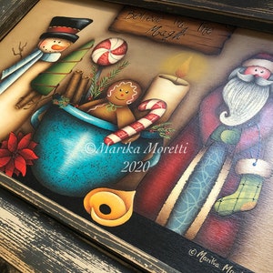 Può includere: Opera d'arte natalizia dipinta a mano in una cornice nera anticata. L'immagine presenta un pupazzo di neve, Babbo Natale, una tazza con pan di zenzero e caramelle e la scritta "Believe in the Magic". L'opera è firmata "Marika Moretti 2020".