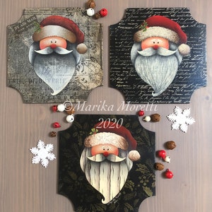 Può includere: Tre cartelli in legno con un'immagine dipinta di Babbo Natale su ciascuno. I cartelli sono decorati con uno sfondo bianco e nero e hanno un bordo a festoni. I cartelli sono disposti a forma di triangolo su una superficie in legno.