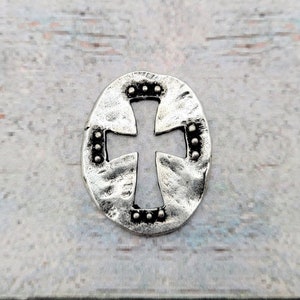 May include: A silver charm with a cross cut-out design. The cross is surrounded by a circle of small dots.