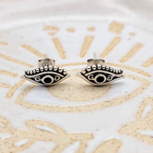 May include: A pair of silver evil eye earrings with black onyx stones. The earrings are small and delicate, and they have a simple design.