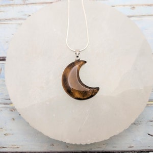 May include: A silver chain necklace with a crescent moon pendant made of tiger's eye gemstone.