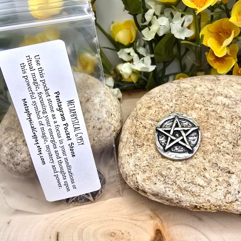 Puede incluir: Una piedra de bolsillo pentagrama plateada sobre una roca texturizada de color marr&oacute;n claro. La piedra es una estrella de cinco puntas dentro de un c&iacute;rculo. Una peque&ntilde;a bolsa de pl&aacute;stico con una etiqueta blanca y texto es visible.
