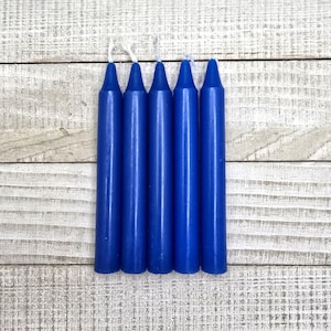 May include: A set of five cylindrical taper candles in a solid deep blue colour. Each candle features a smooth, uniform wax surface and a pointed top with a short, white cotton wick extending from the centre of the tip of each individual candle.