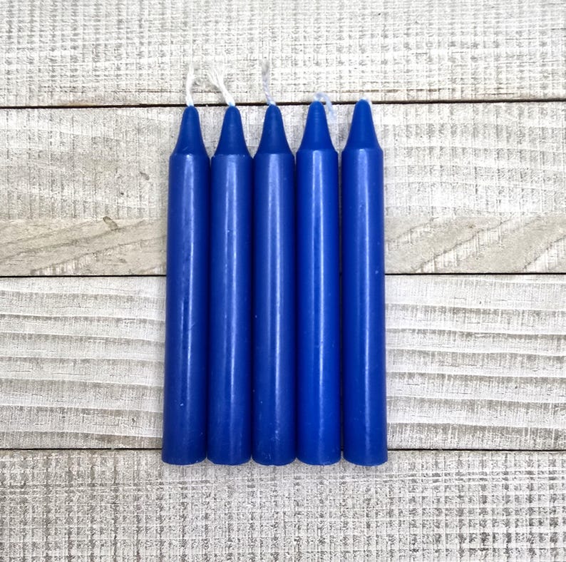 May include: A set of five cylindrical taper candles in a solid deep blue colour. Each candle features a smooth, uniform wax surface and a pointed top with a short, white cotton wick extending from the centre of the tip of each individual candle.
