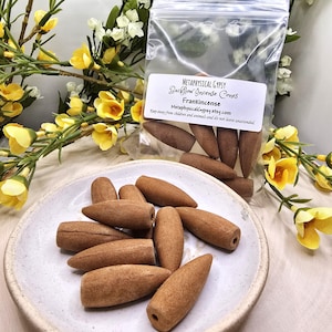 May include: Brown backflow incense cones in a white ceramic dish. The cones are arranged in a pile and are ready to be burned. The cones are labeled "Frankincense" and are sold by Metaphysical Gypsy.
