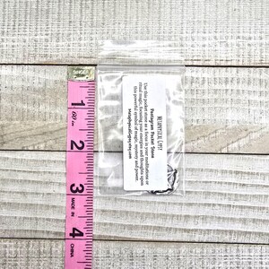 Puede incluir: Una peque&ntilde;a bolsa de pl&aacute;stico transparente que contiene una piedra de bolsillo con pentagrama plateado. Una cinta m&eacute;trica rosa muestra que la bolsa mide aproximadamente 5 cm de largo. El texto en una etiqueta blanca dice "METAPHYSICAL GYPSY Pentagram Pocket Stone".