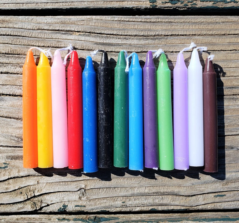 May include: A set of twelve cylindrical taper candles in a variety of solid colours including orange, yellow, pink, red, blue, black, green, light blue, purple, lime green, lavender, white, and brown, each featuring a white cotton wick at the top.