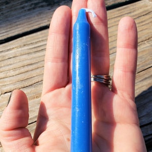 May include: A solid blue taper candle with a smooth, cylindrical body and a pointed top. The candle features a single white cotton wick protruding from the centre of the top. The wax has a consistent, vibrant blue colour throughout its entire length.