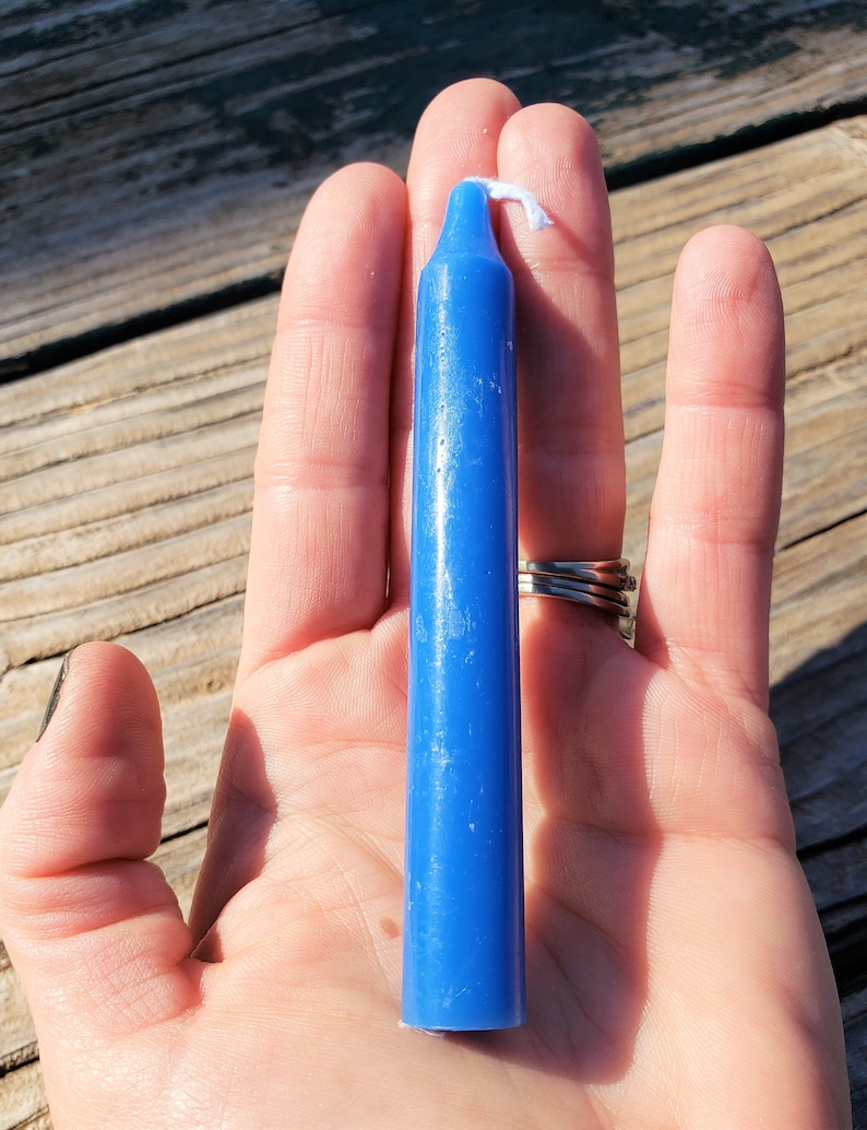 May include: A solid blue taper candle with a smooth, cylindrical body and a pointed top. The candle features a single white cotton wick protruding from the centre of the top. The wax has a consistent, vibrant blue colour throughout its entire length.