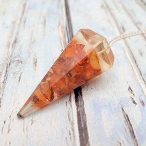 May include: A clear quartz crystal pendulum with a silver chain. The crystal is filled with small, orange carnelian stones.