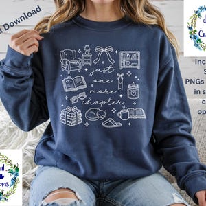 May include: A navy blue sweatshirt with a white graphic design featuring the text "just one more chapter" and illustrations of books, glasses, and a cat. The design also includes the text "Joyful Creations" and "Includes: SVG PNGs (300dpi) in several color options."