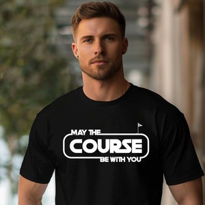 Puede incluir: Camiseta negra con un gráfico blanco que dice "Que el campo esté contigo" con un icono de bandera de golf.