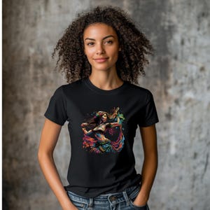 May include: Black t-shirt with a colorful graphic print of a woman dancing. The woman is wearing a colorful outfit and has long flowing hair.