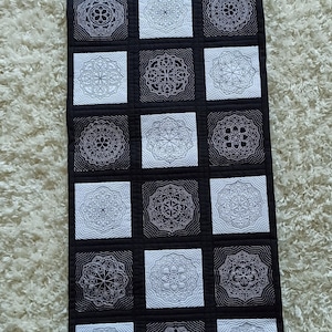 May include: Black and white quilt featuring a repeating pattern of intricate mandala designs. The quilt is made up of squares with alternating black and white backgrounds.