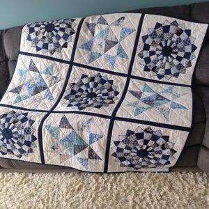 May include: A handmade quilt with a patchwork design. The quilt features nine squares with alternating star and circular patterns in shades of blue and white. The quilt is draped over a grey sofa.