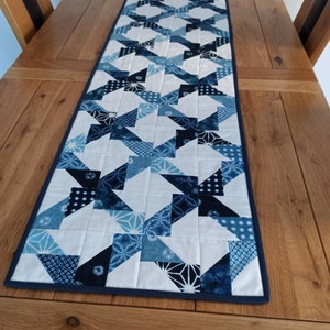 May include: A blue and white table runner with a geometric pattern. The runner is made of fabric and has a dark blue border.