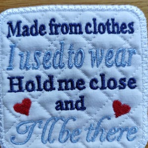 May include: A square white quilted fabric patch with embroidered text that reads Made from clothes I used to wear Hold me close and I'll be there. The text is in dark blue and light blue, accented by two small red embroidered hearts.