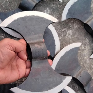 May include: A group of six double-headed axes with a black metal finish and a white edge. The axes are arranged in a pile on a gray concrete surface.