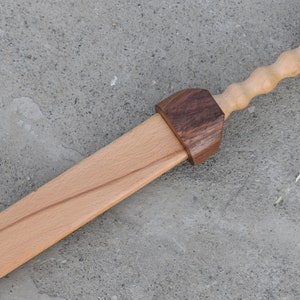 K&ouml;nnte beinhalten: Ein h&ouml;lzernes Spielzeugschwert mit einem braunen Holzgriff und einem runden Knopf am Ende. Das Schwert ist aus hellem Holz gefertigt und hat eine nat&uuml;rliche Oberfl&auml;che.