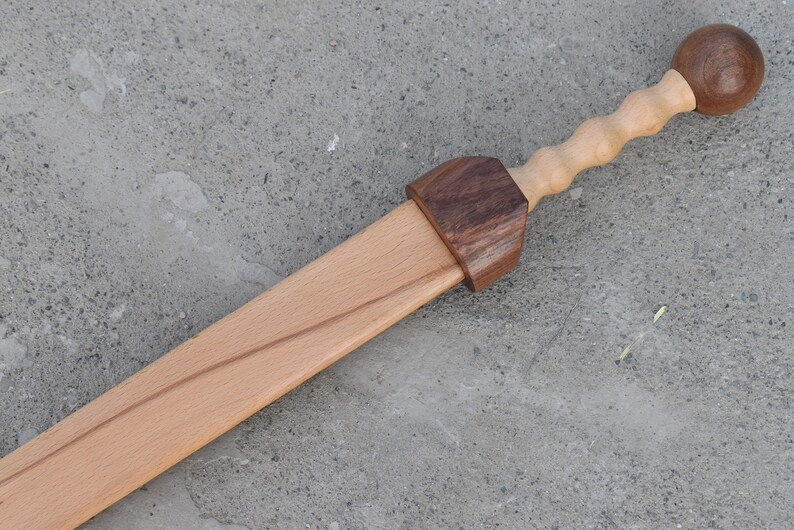 K&ouml;nnte beinhalten: Ein h&ouml;lzernes Spielzeugschwert mit einem braunen Holzgriff und einem runden Knopf am Ende. Das Schwert ist aus hellem Holz gefertigt und hat eine nat&uuml;rliche Oberfl&auml;che.