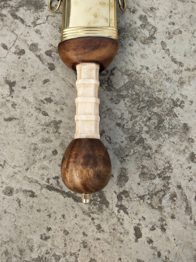 May include: Close-up of the pommel of a sword with a wooden handle and a brass hilt. The handle is made of light brown wood and has a white bone-like grip. The pommel is rounded and also made of wood.