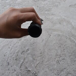 May include: A black rubber drain stopper with a round opening. The stopper is being held by a hand.