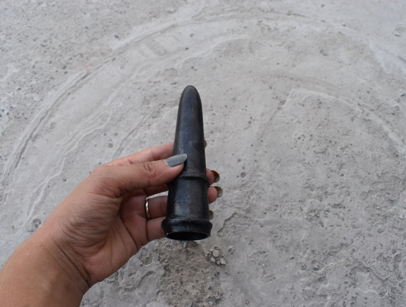 May include: A black, cone-shaped, wooden object with a smooth surface. The object is held in a hand.