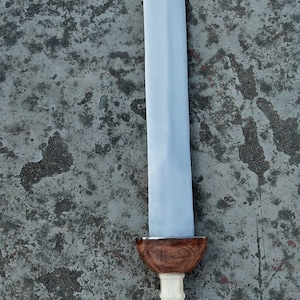 May include: A silver sword with a wooden handle. The handle has a white, textured grip and a brown, rounded pommel.