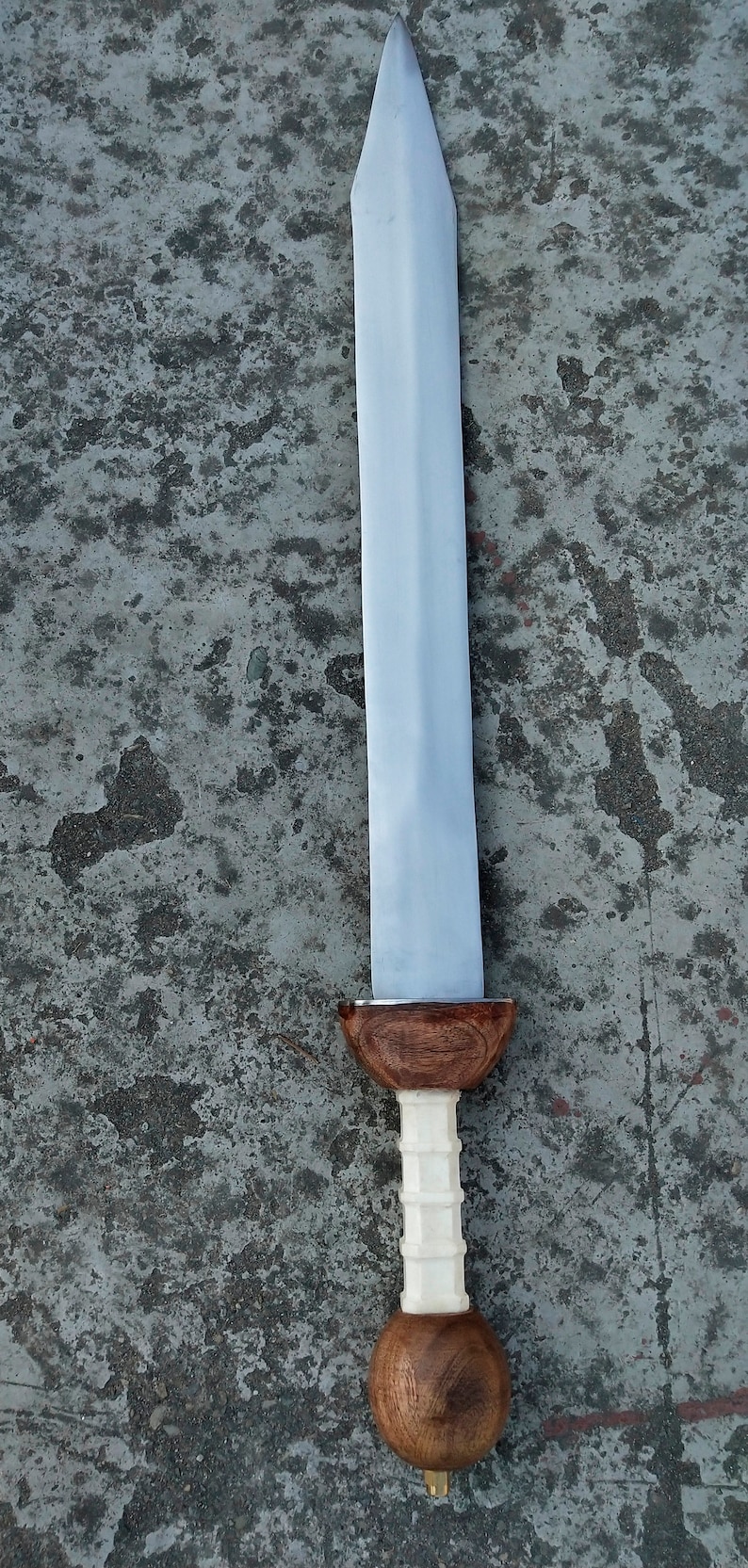 May include: A silver sword with a wooden handle. The handle has a white, textured grip and a brown, rounded pommel.