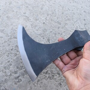 May include: A black hand axe with a curved blade and a wooden handle. The axe is held in a hand.
