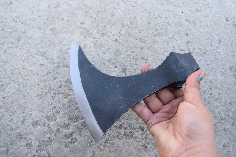 May include: A black hand axe with a curved blade and a wooden handle. The axe is held in a hand.